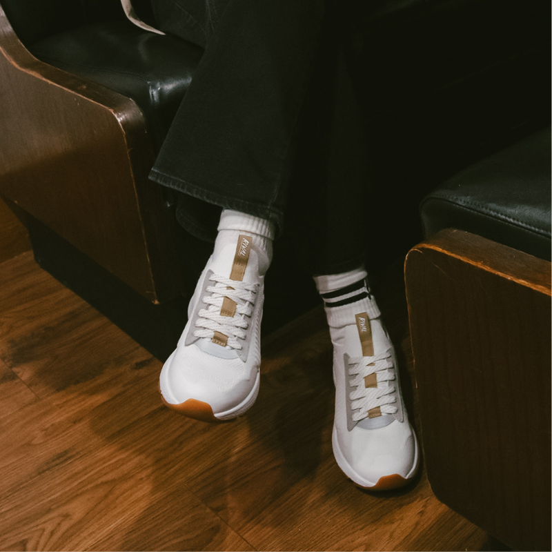 White sneakers with brown accents worn indoors on a wooden floor.